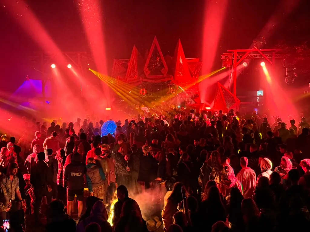 Crowd of people at night concert with red and yellow stage lights and blue light sphere.