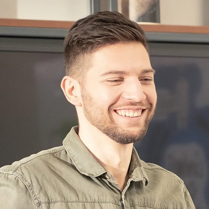 Man with short dark hair and a beard, smiling, wearing a green shirt.
