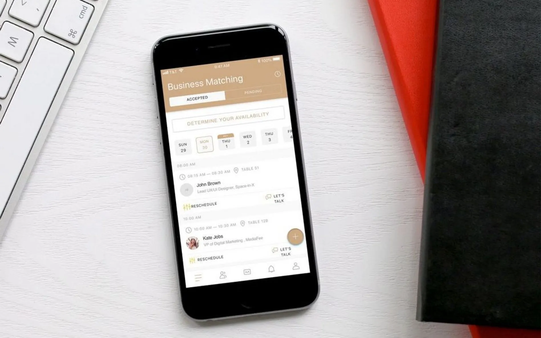 Smartphone on a white desk next to a keyboard, with the screen showing the Business Matching application with a list of meetings and availability calendar.