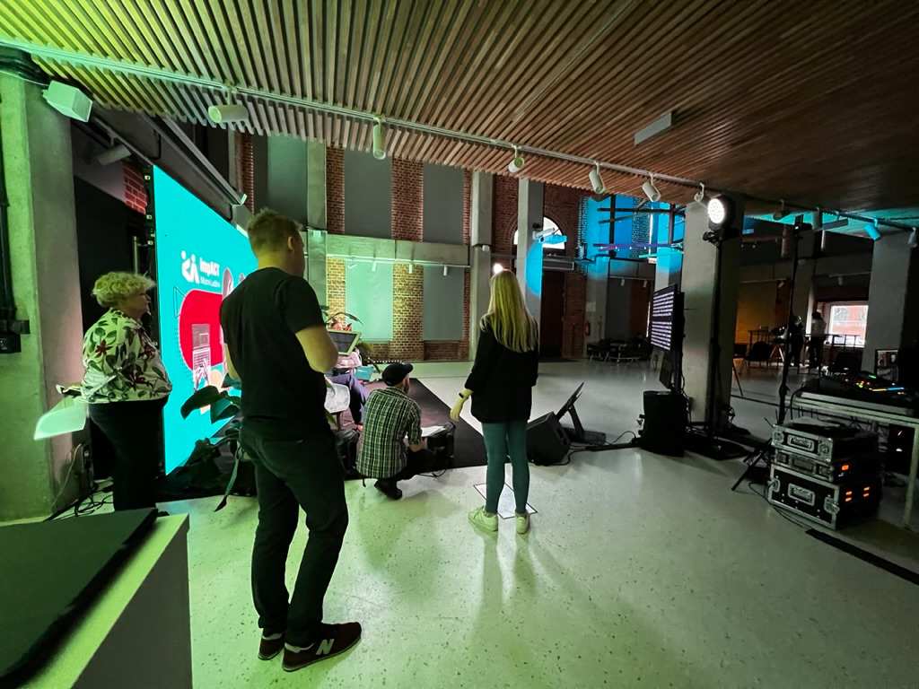 Group of people standing and talking in modern interior with large LED screen and studio lighting.