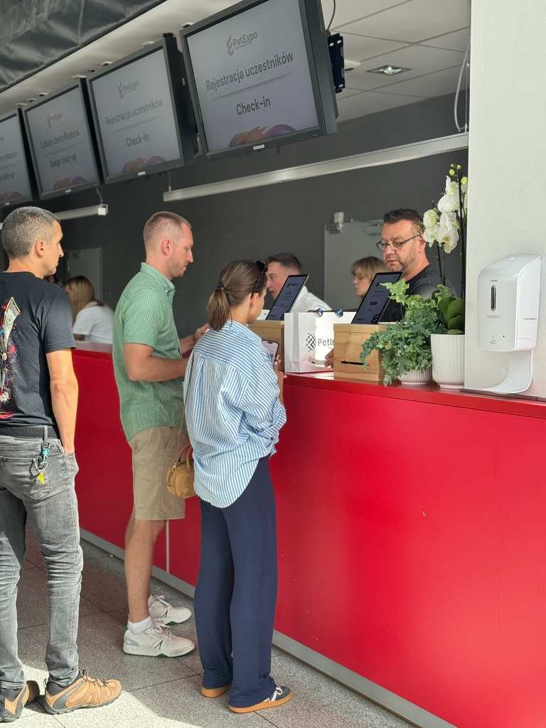 People standing at red registration desk for PetExpo event with displays showing 'Participant Registration Check-in'.
