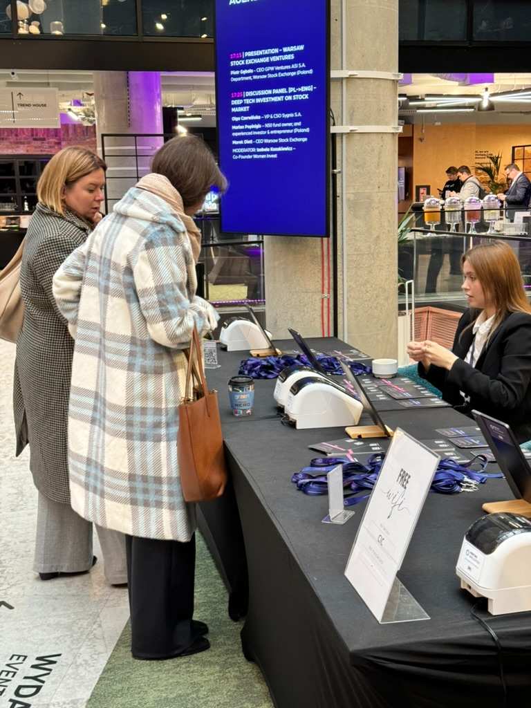 Two women standing at registration table at event, seated woman on other side helping them with registration.