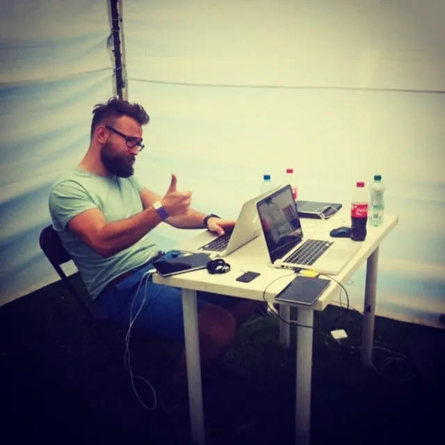 Man sitting at table with laptops, giving thumbs up in white tent.