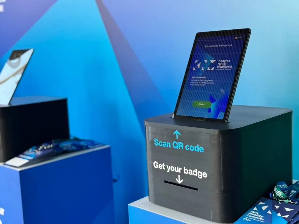 Registration station with tablet displaying New Mobility Congress and text 'Scan QR code, collect ID badge'.