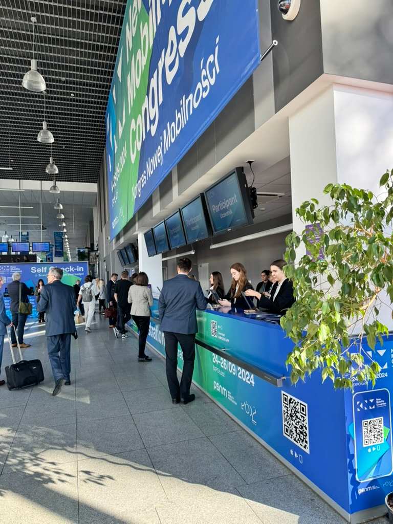 People registering and talking at reception desks at conference or trade show in bright hall.